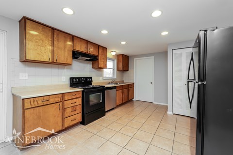 A kitchen with a black refrigerator and wooden cabinets.