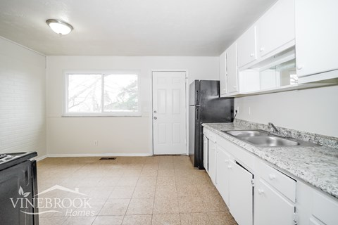 A kitchen with white cabinets and a black fridge.