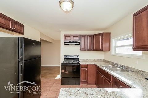 A kitchen with brown cabinets and a black fridge.