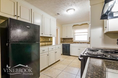 A kitchen with a black fridge and a black stove top.