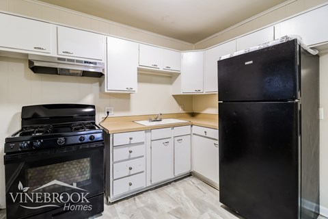 A kitchen with a black fridge and stove and white cabinets.