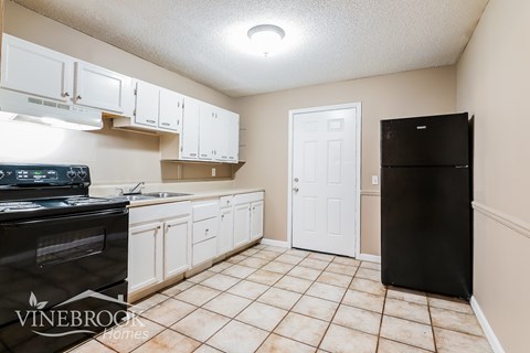 A kitchen with a black refrigerator and white cabinets.