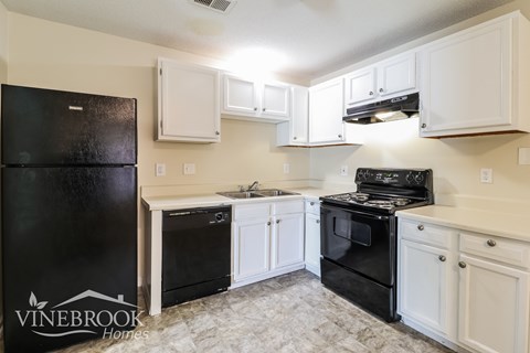 A black fridge and oven in a kitchen with white cabinets.