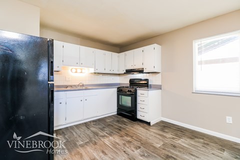 A kitchen with white cabinets and a black fridge.