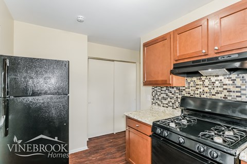 A kitchen with a black stove top oven and a black fridge with a Vinebrook Homes sign on it.