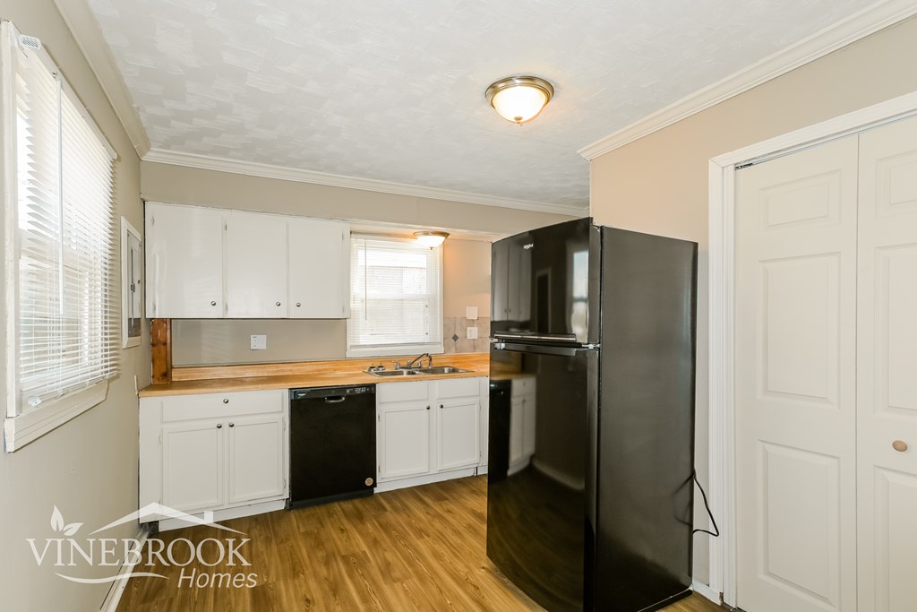 A kitchen with a black refrigerator and white cabinets.