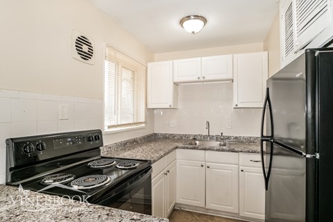 A kitchen with a black stove top oven, black refrigerator, and white cabinets.