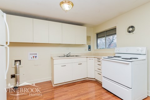 A white kitchen with a fridge, stove, and sink.