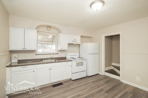 A kitchen with white cabinets and appliances, and a logo that reads "Vinebrook Homes".
