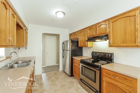 A kitchen with wooden cabinets and a Vinebrook Homes logo.