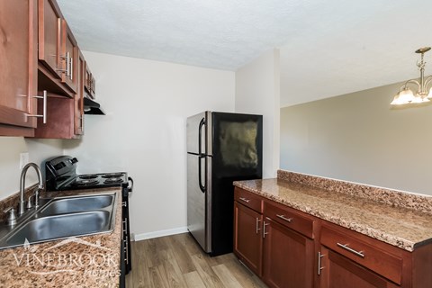 A kitchen with a black refrigerator and brown cabinets.