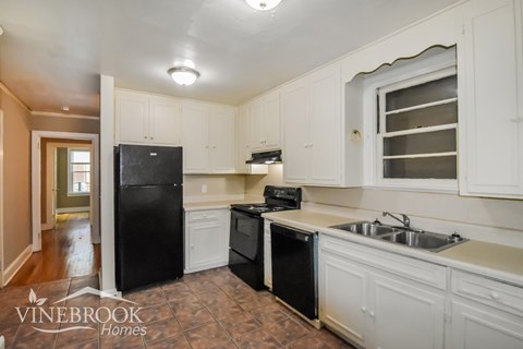 A kitchen with a black fridge and black dishwasher with white cabinets.