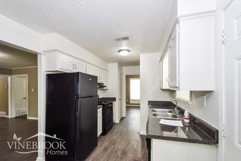 A kitchen with a black fridge and white cabinets.