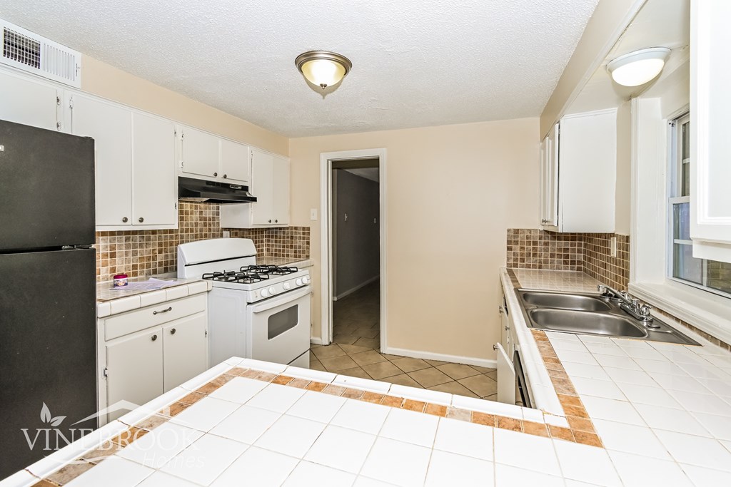 A kitchen with a black refrigerator and white cabinets.