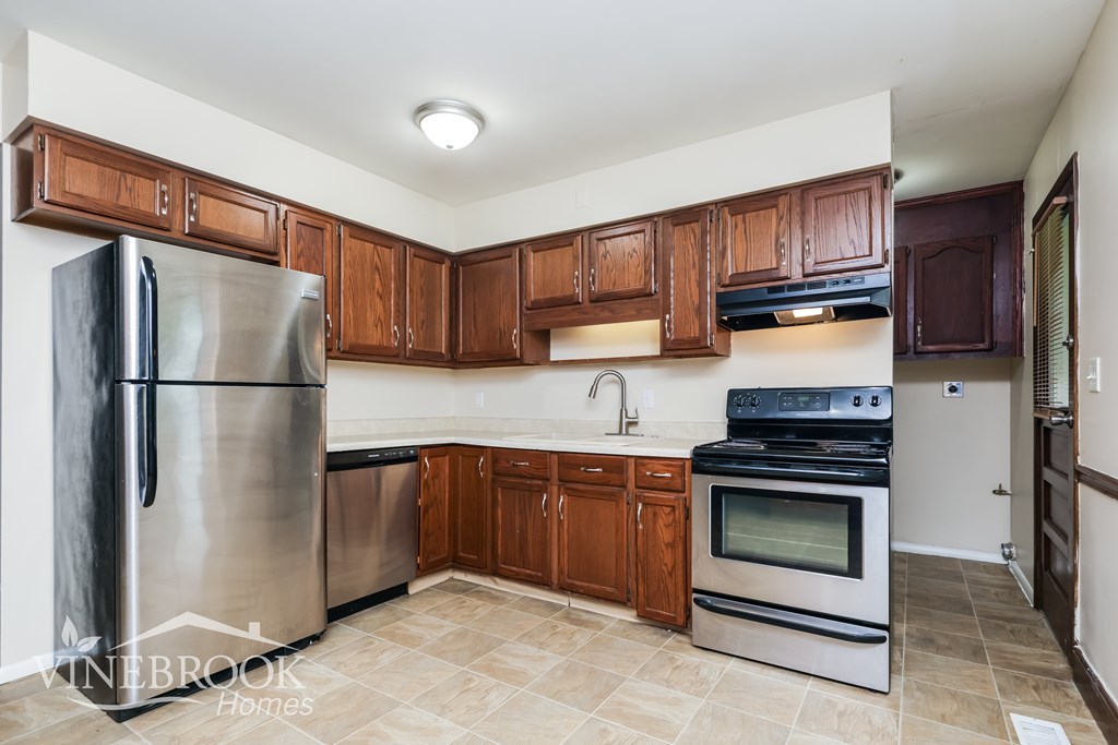 A kitchen with a stainless steel refrigerator and wooden cabinets.