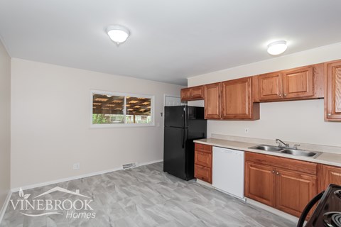 A kitchen with a black refrigerator, wooden cabinets, and a white sink.