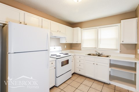 A white kitchen with a refrigerator, stove, and sink.