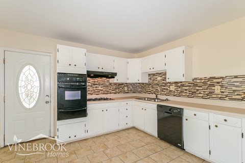 A kitchen with white cabinets and a stone backsplash.