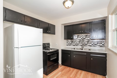 A kitchen with black cabinets and a white refrigerator.