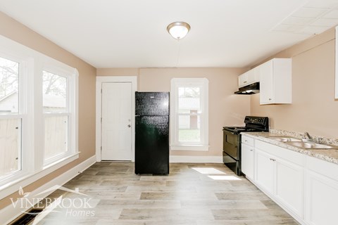 A kitchen with a black fridge, white cabinets, and a window.