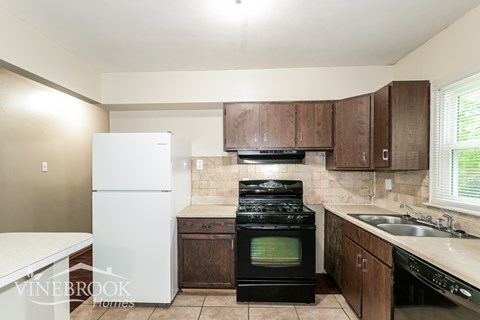 A kitchen with a white fridge, black stove and brown cabinets.