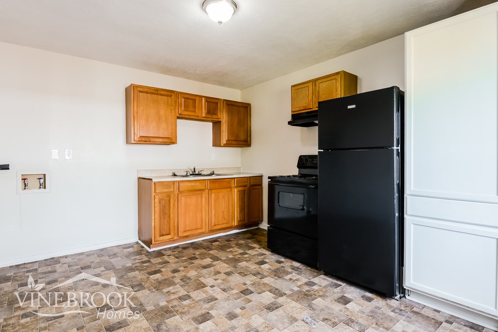 A kitchen with a black fridge and wooden cabinets.