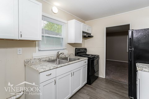 A kitchen with white cabinets and a black refrigerator.