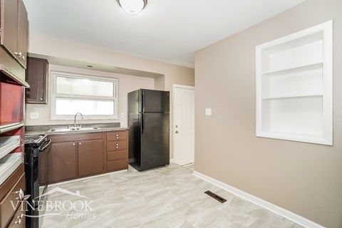 A kitchen with a black refrigerator and brown cabinets.