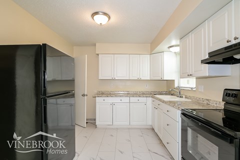 A kitchen with white cabinets and a black refrigerator.