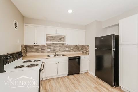 A kitchen with a black refrigerator and a white stove top oven.