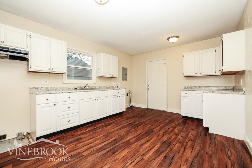 A kitchen with white cabinets and a wooden floor.