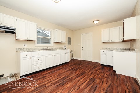 A kitchen with white cabinets and a wooden floor.