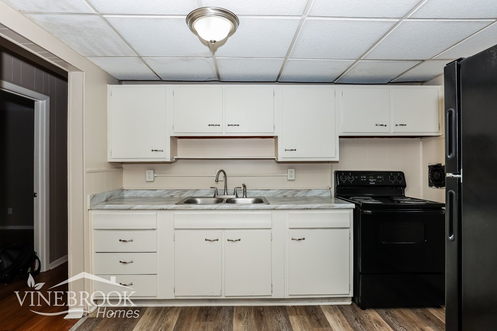 A kitchen with white cabinets and a black refrigerator.
