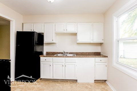A kitchen with white cabinets and a black refrigerator.