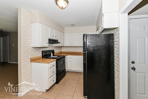 A black refrigerator in a kitchen with white cabinets.