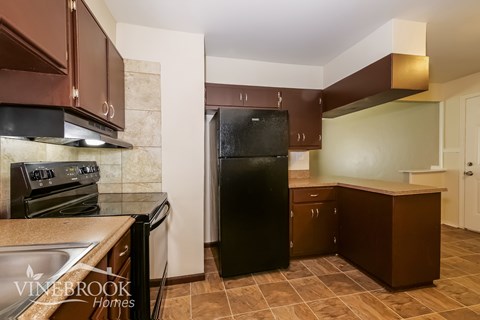 A kitchen with brown cabinets and a black refrigerator.
