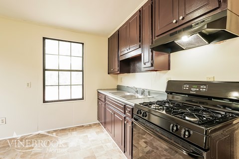 A kitchen with a black stove top oven and brown cabinets.