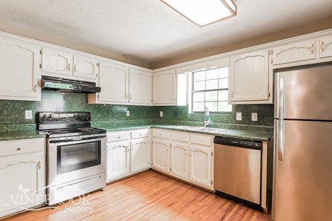 A kitchen with white cabinets and a green backsplash.