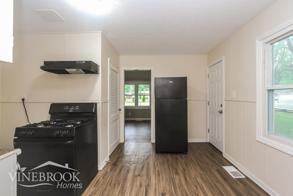 A kitchen area with a black fridge and stove, and a window with a view of trees.