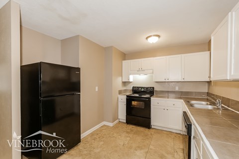 A kitchen with a black refrigerator and white cabinets.
