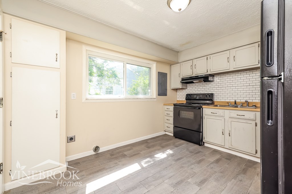 A kitchen with a black refrigerator and wooden cabinets.