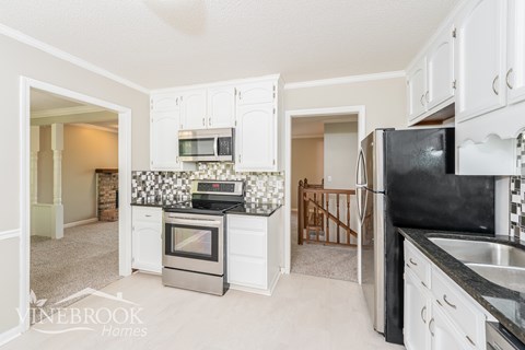 A kitchen with white cabinets and a black fridge.