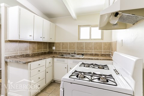 A white kitchen with a stove top oven and cabinets.