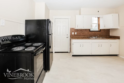 A black Vinebrook Homes refrigerator is in a kitchen with white cabinets.