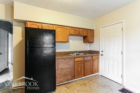 A black fridge in a kitchen with wooden cabinets and a white door.