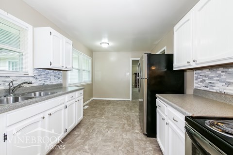 A kitchen with white cabinets and a black refrigerator.