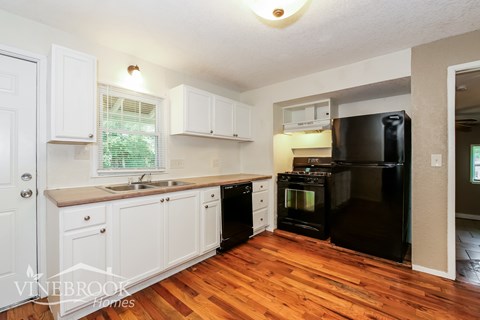 A kitchen with white cabinets and a black fridge.