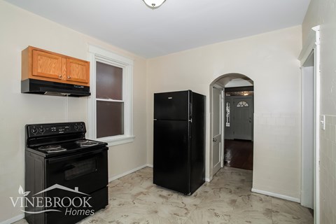 A black refrigerator sits in a kitchen with a black stove and wooden cabinets.