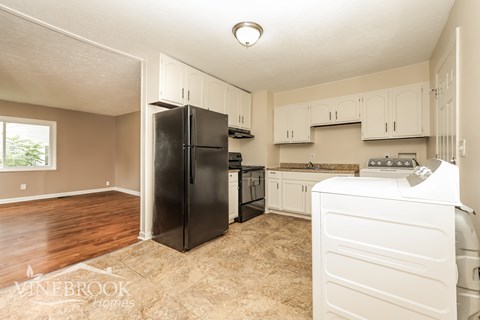 A kitchen with a black fridge and white washing machine.
