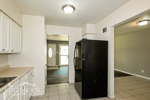 A black refrigerator in a kitchen with white cabinets and a tiled floor.